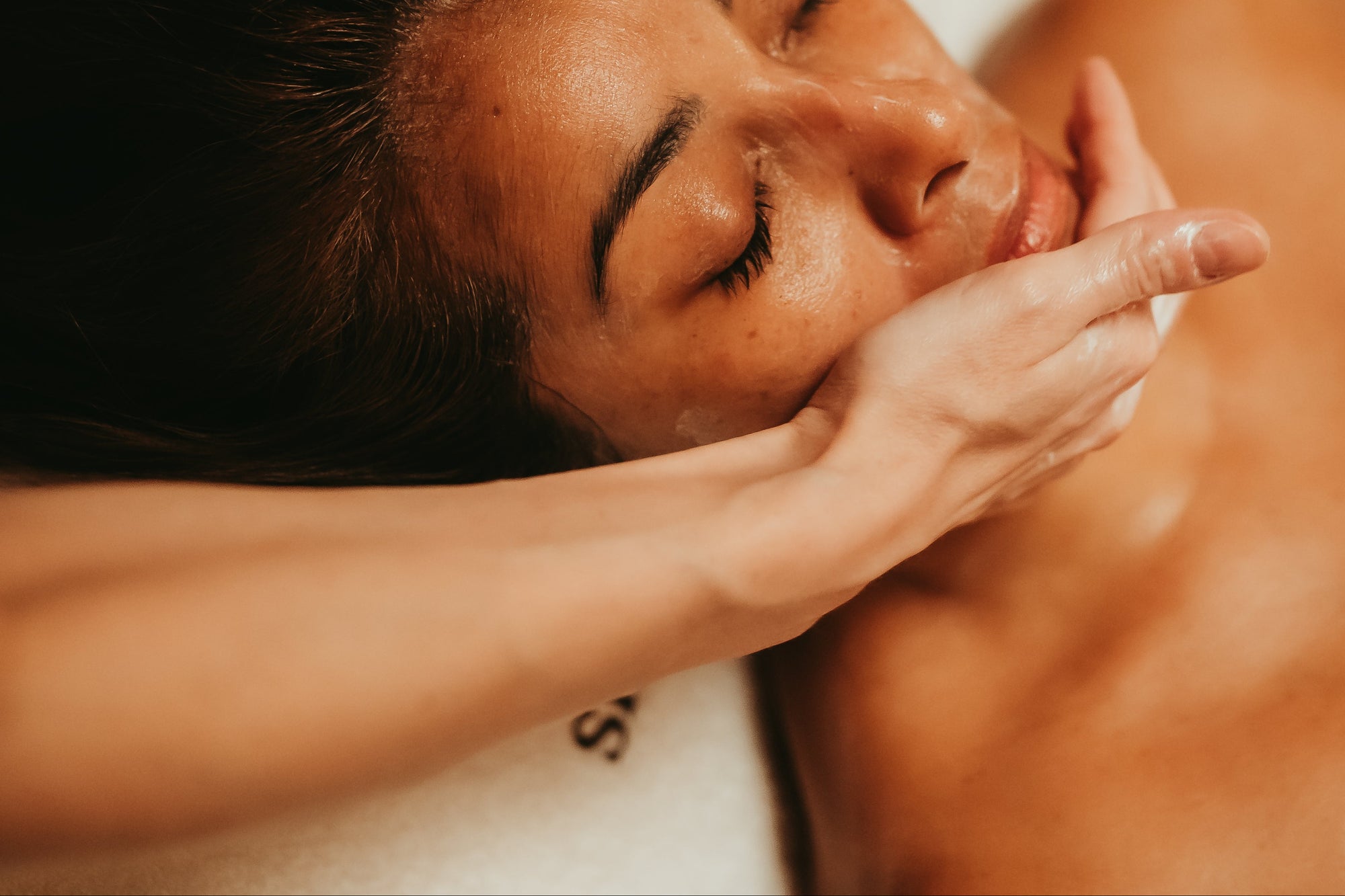 Person receiving a facial massage with a focus on the hands and face.