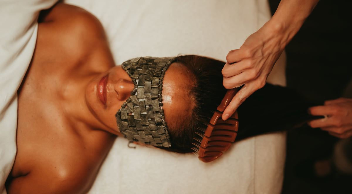 Client receiving a head massage with a wooden brush on a white towel.